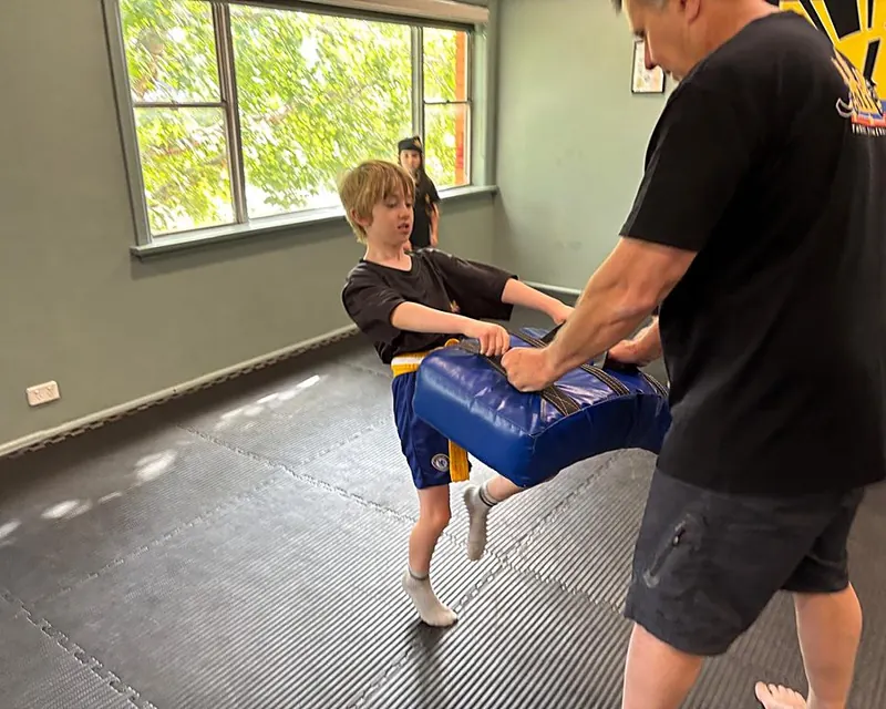 Young student practising a kick on a pad held by an instructor